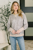 Woman wearing a grey leopard print pullover with a ribbed crew neck and drop shoulders.