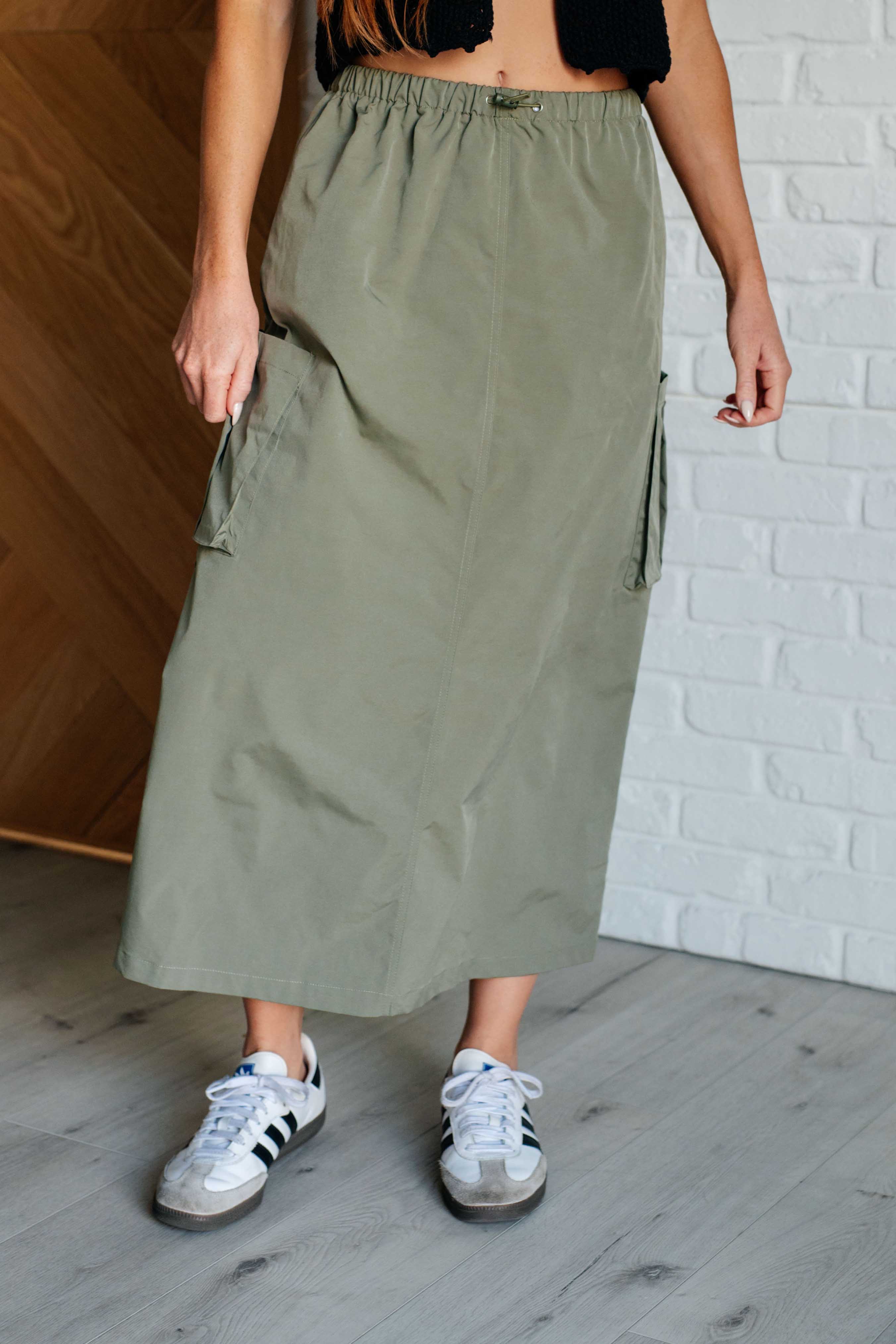 Woman wearing a green skirt and white sneakers against a white brick wall.