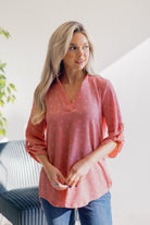 A woman wearing a pink top with a half-button design and quarter sleeves, standing in a bright room.