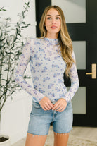 Woman wearing a floral long-sleeve top and denim shorts indoors.