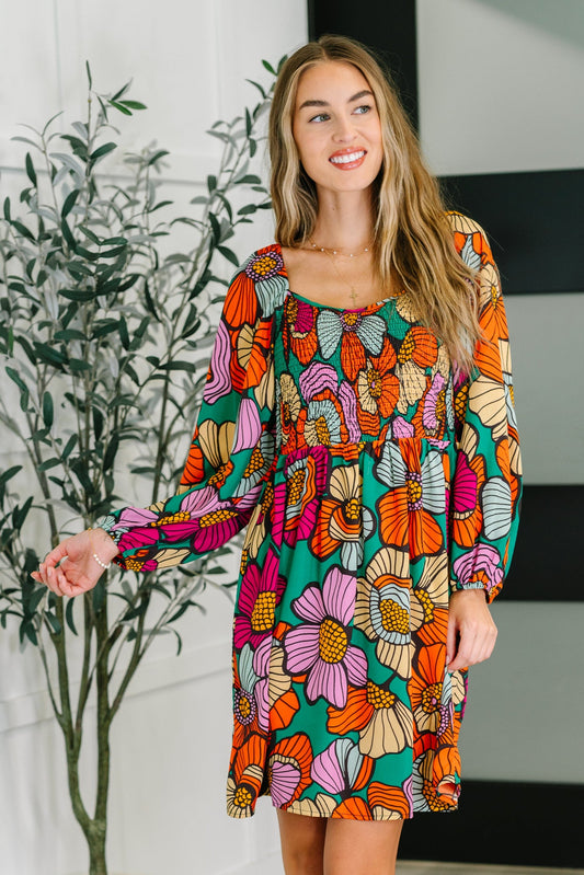 Woman wearing a colorful floral dress standing indoors with a plant in the background