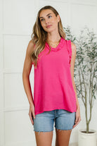 A model wearing a sleeveless hot pink tank top with ruffle detail at the neckline, paired with denim shorts.