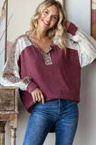 Woman wearing a maroon shirt top with white and leopard print details, blue jeans,.