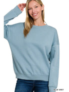 A woman wearing a dusty teal pullover with a relaxed drop shoulder fit and banded neckline.