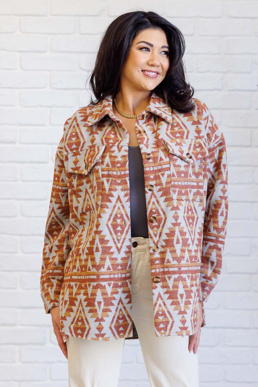 Model wearing a rust Aztec patterned shacket with a collared neckline and button front.
