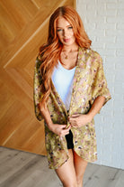 Woman wearing a floral kimono over a white top and black shorts in a room with wooden and brick walls.