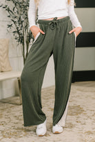 Model wearing high-waisted olive ribbed knit pants with a drawstring waist and side pockets.