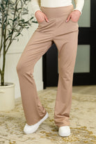 Woman wearing beige pants and white shoes in a room with a plant and rug.
