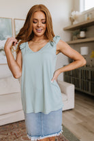 Woman wearing a light blue sleeveless top and denim skirt in a living room.