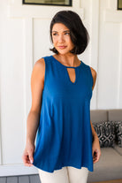 Woman wearing a blue sleeveless tank top with a cutout design, standing in a room with a white wall and gray couch