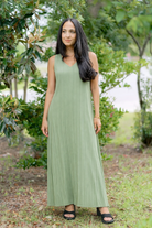 A woman wearing a sage-colored, textured V-neck maxi dress with a flowing silhouette, standing outdoors.