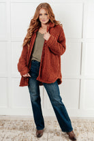 Woman wearing a brown sherpa jacket with a collared neckline and snap button closure.