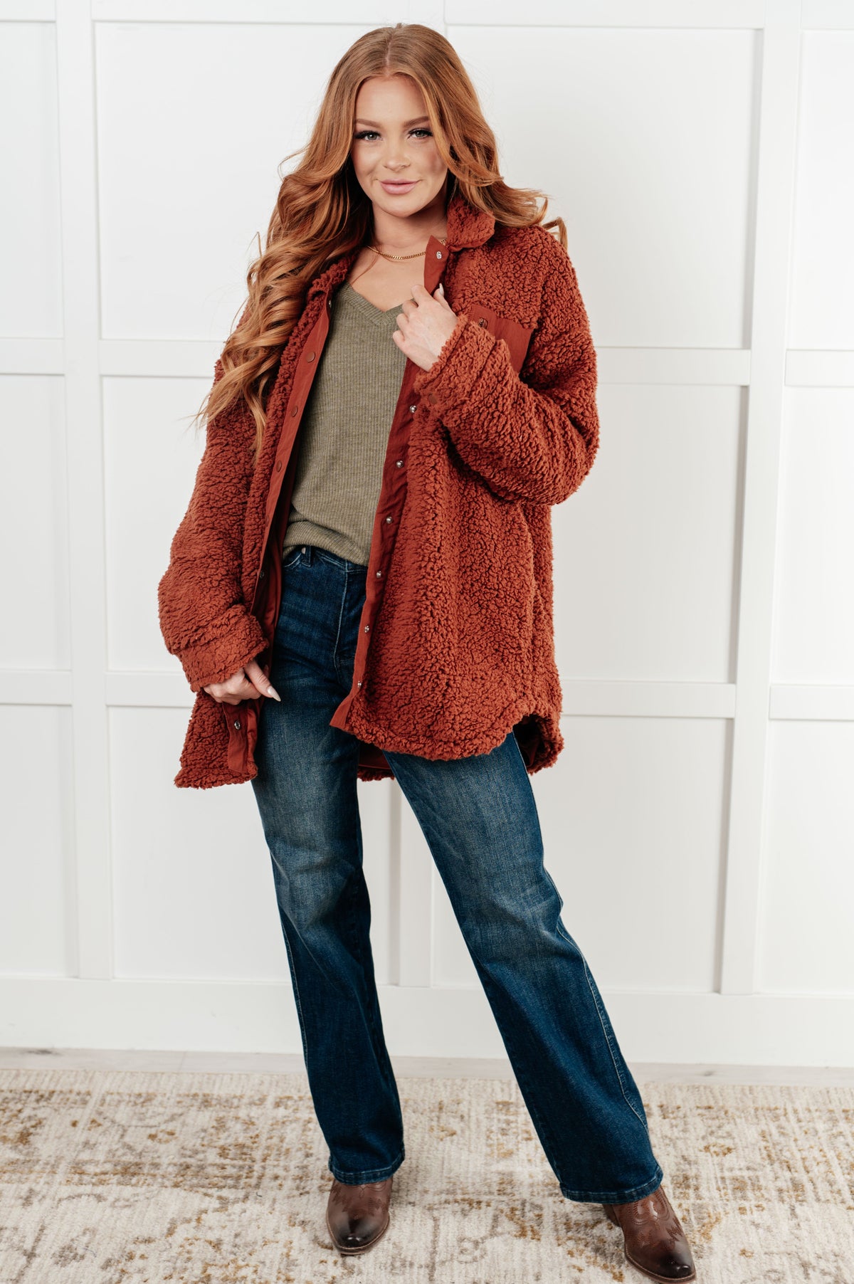Woman wearing a brown sherpa jacket with a collared neckline and snap button closure.