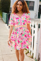 A woman standing on the sidewalk wearing a short-sleeved babydoll dress with a floral print and ric rac details.