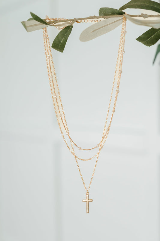 Gold necklace with a cross pendant on a light gray background