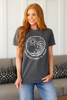 A woman smiling and wearing a gray t-shirt with a graphic that reads 'HAPPINESS COMES IN WAVES' and features a sun and waves design.