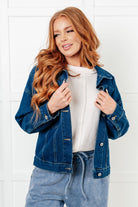 Woman wearing a blue denim jacket and jeans against a white tiled wall.