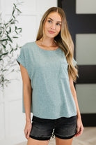 A woman wearing an ash jade colored basic tee with short dolman sleeves and a round neckline, paired with black denim shorts.