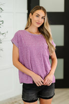A woman wearing a light plum colored basic tee with a round neckline, short dolman sleeves, and a banded hem. She has patch pockets on the front.