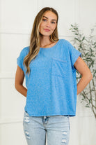A woman wearing a heathered ocean blue basic tee with a round neckline, short dolman sleeves, and a front pocket.