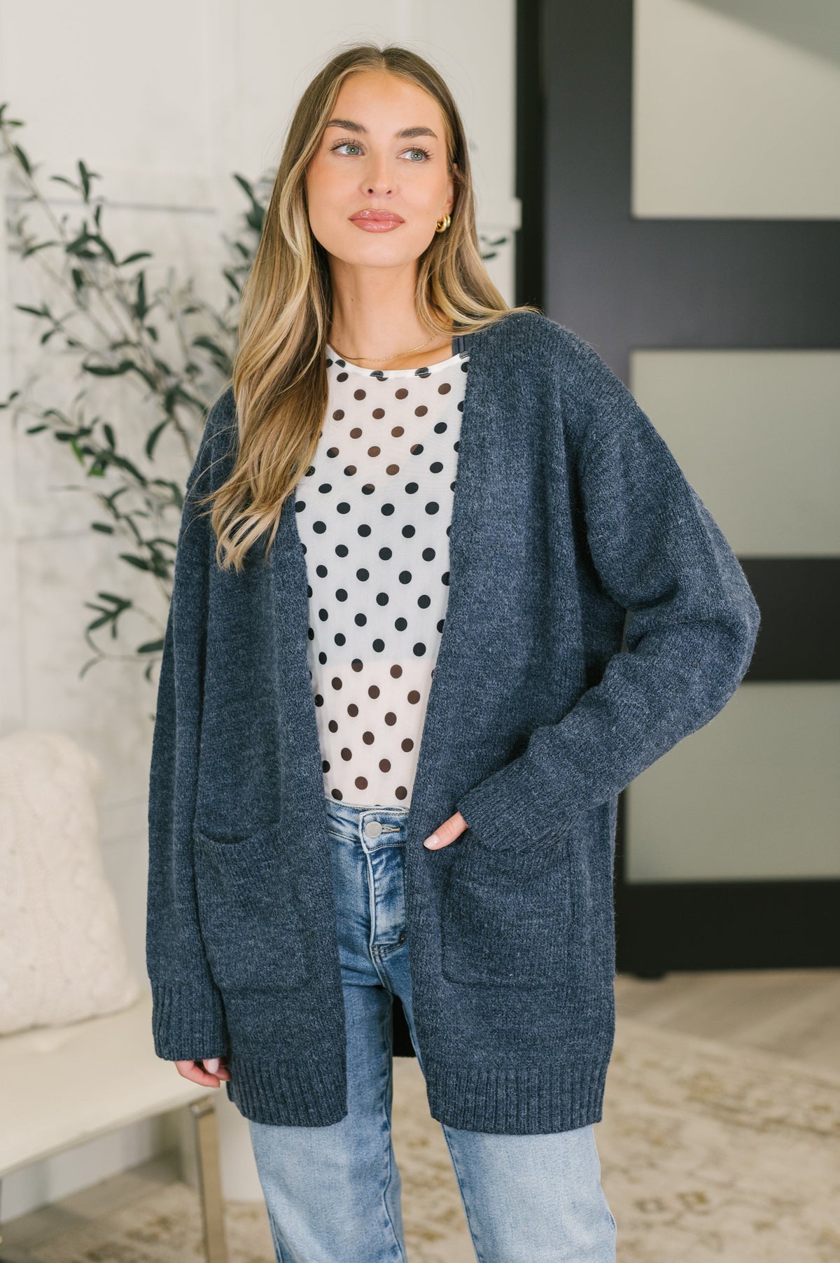 A woman wearing a midnight blue open front cardigan with ribbed cuffs and hemline, paired with a polka dot top and jeans.