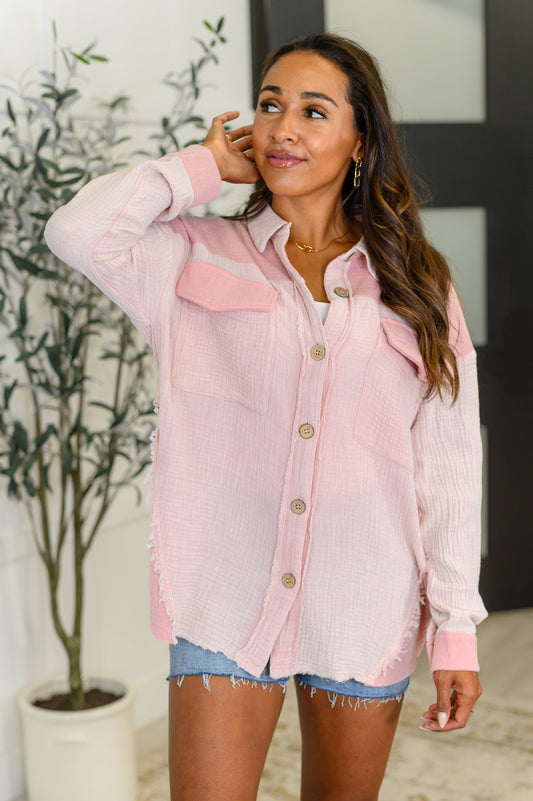 Woman wearing a light pink button-up shirt with denim shorts indoors.