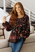 Woman wearing a patterned top and jeans sitting on a couch.