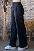 Woman wearing black wide-leg pants with a brick wall and decorative items in the background