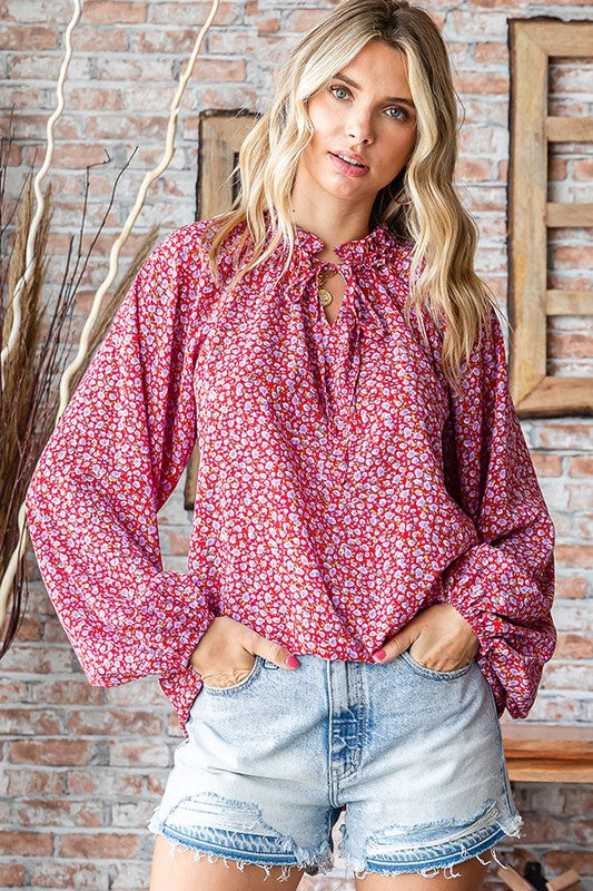 Woman wearing a red floral blouse and denim shorts against a brick wall.