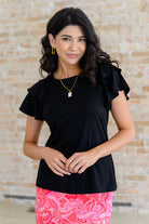 A woman wearing a black flutter sleeve tee with a round neckline and a pink skirt.