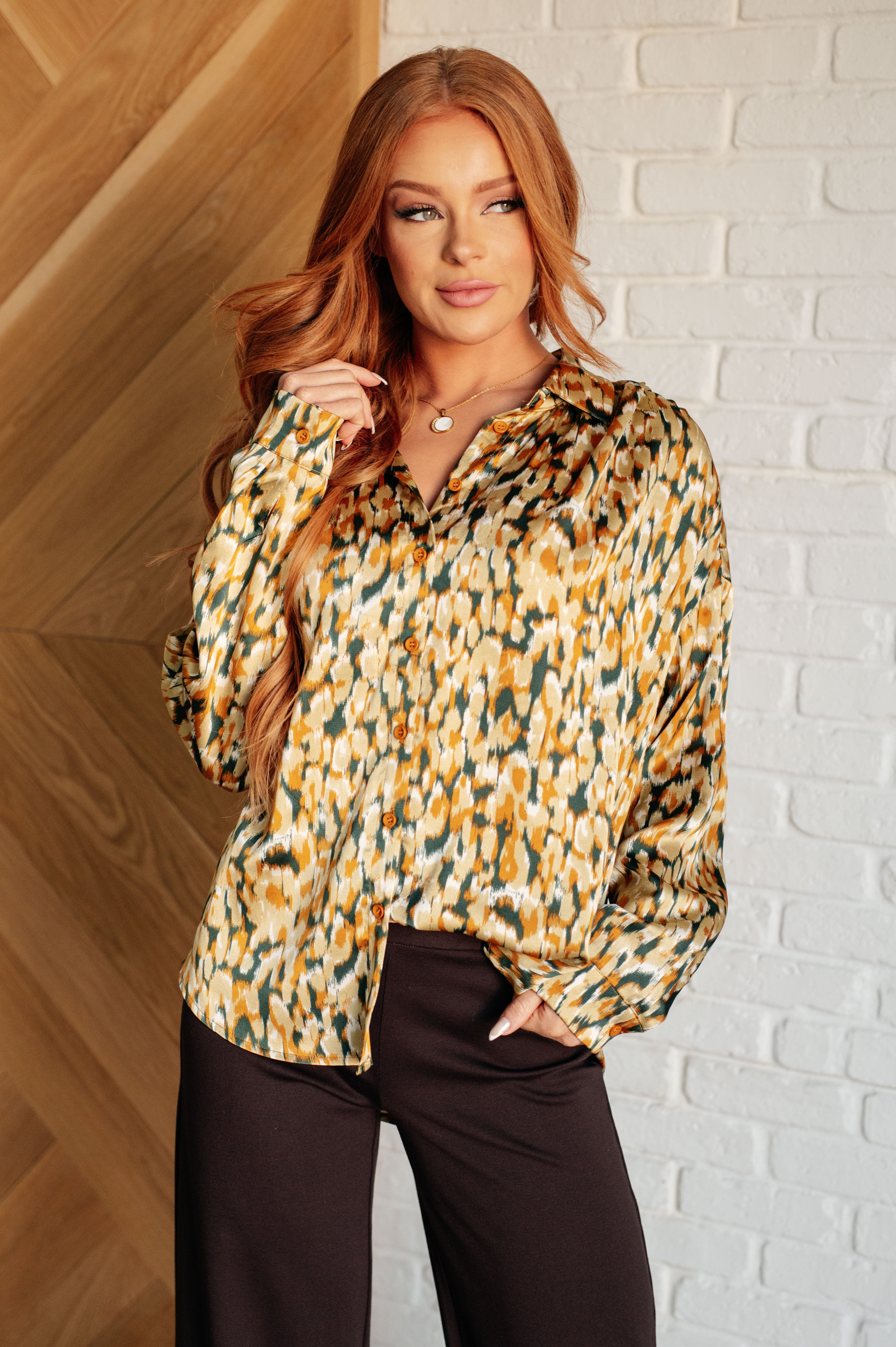 Woman wearing a patterned blouse against a white brick wall.