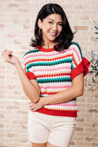 Woman wearing a colorful striped sweater against a brick wall.