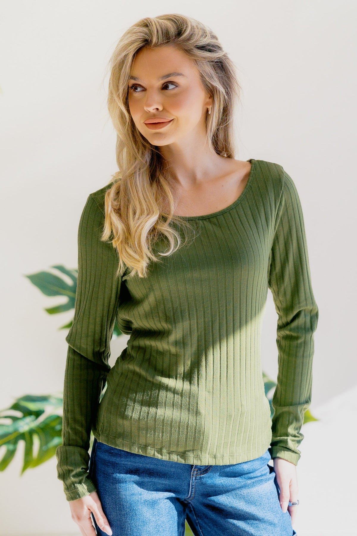 A woman in an olive top with long sleeves and a round neckline, featuring a ribbed texture.