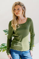 A woman in an olive top with long sleeves and a round neckline, featuring a ribbed texture.