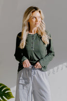Woman wearing an olive green long-sleeve henley top with button details.