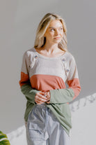 A model wearing a colorblock knit top in cream, mauve, and olive with a round neckline and button details.