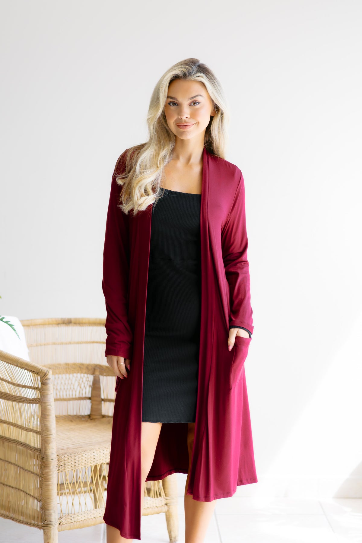 A woman wearing a burgundy open-front cardigan with long sleeves and side pockets.