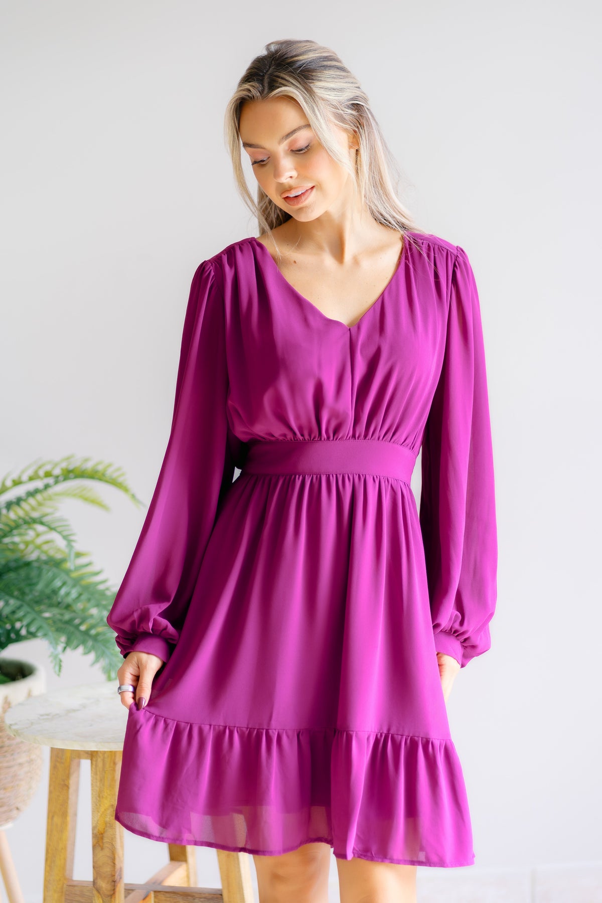 Woman wearing a plum/magenta dress with a V-neckline and long balloon sleeves.