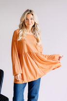 Woman wearing an orange long-sleeve peplum top with a relaxed fit.