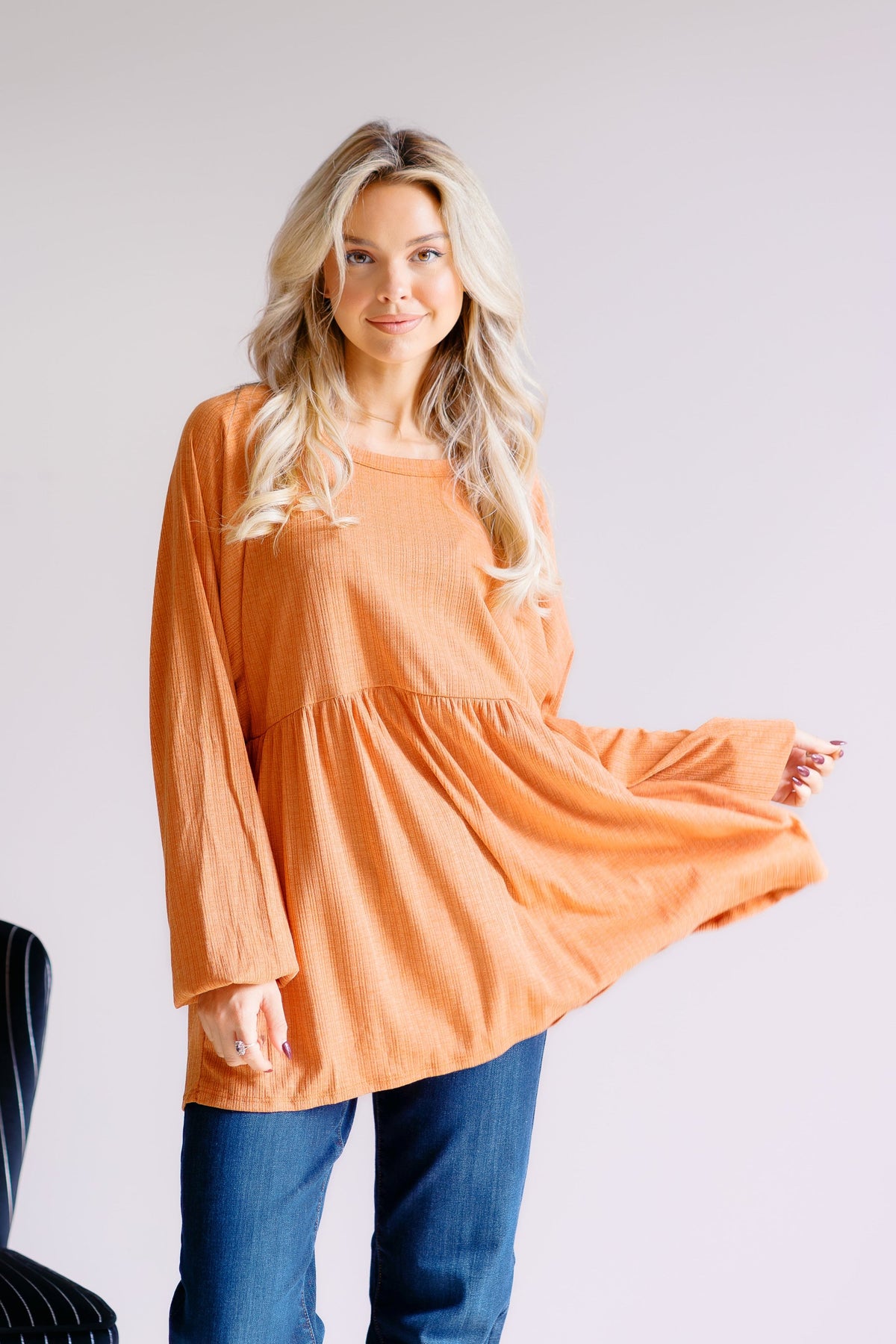 Woman wearing an orange long-sleeve peplum top with a relaxed fit.