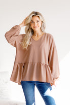A mocha-colored peplum top with balloon sleeves, worn by a woman standing indoors.