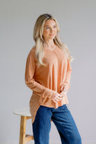A woman wearing a mustard long sleeve top with a v-neck and dolphin hem.