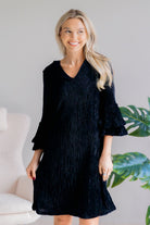 Black dress with shimmering glitter, V-neck, and 3/4 bell sleeves worn by a model.