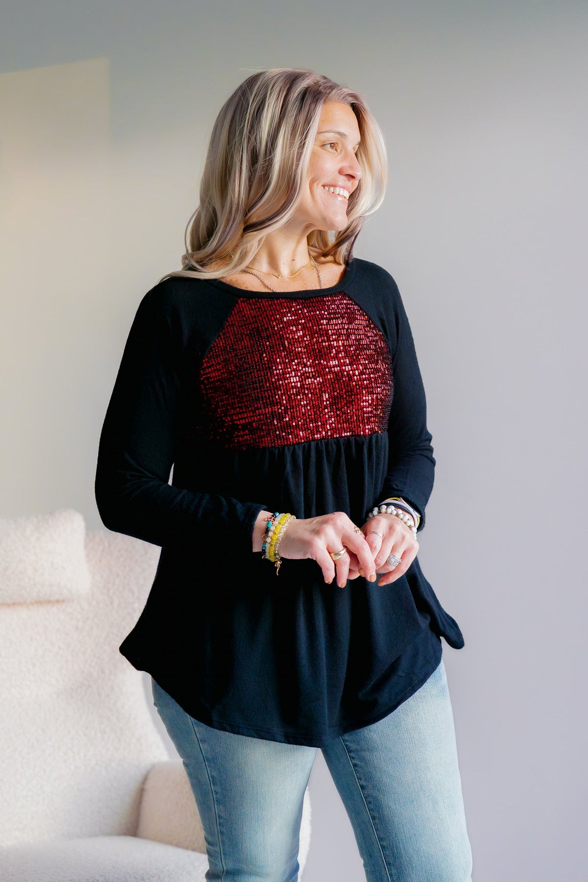 A woman wearing a black tunic with red velvet sequins across the chest, paired with jeans.