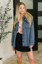 Woman wearing a denim shirt over a floral top and black skirt, standing indoors.