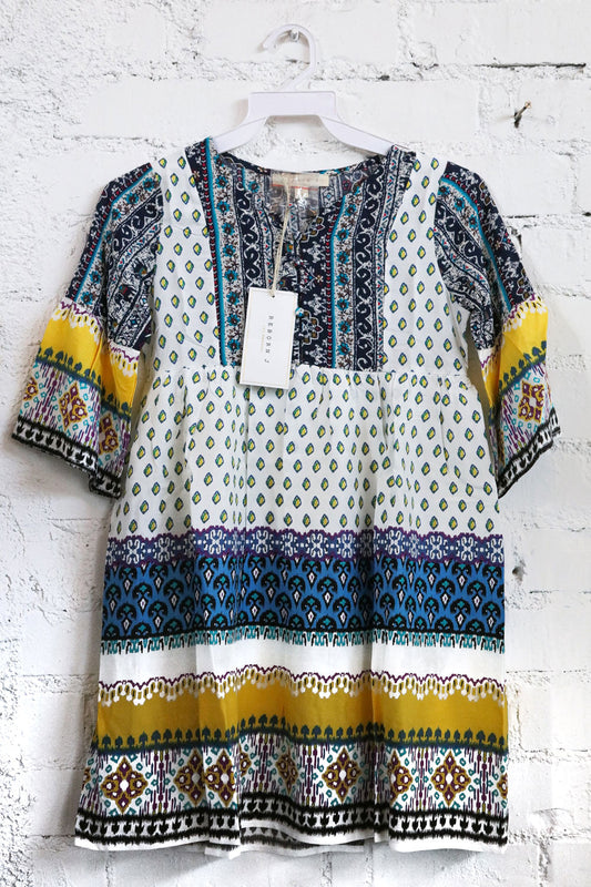 Kids colorful patterned dress on a hanger against a white brick wall.