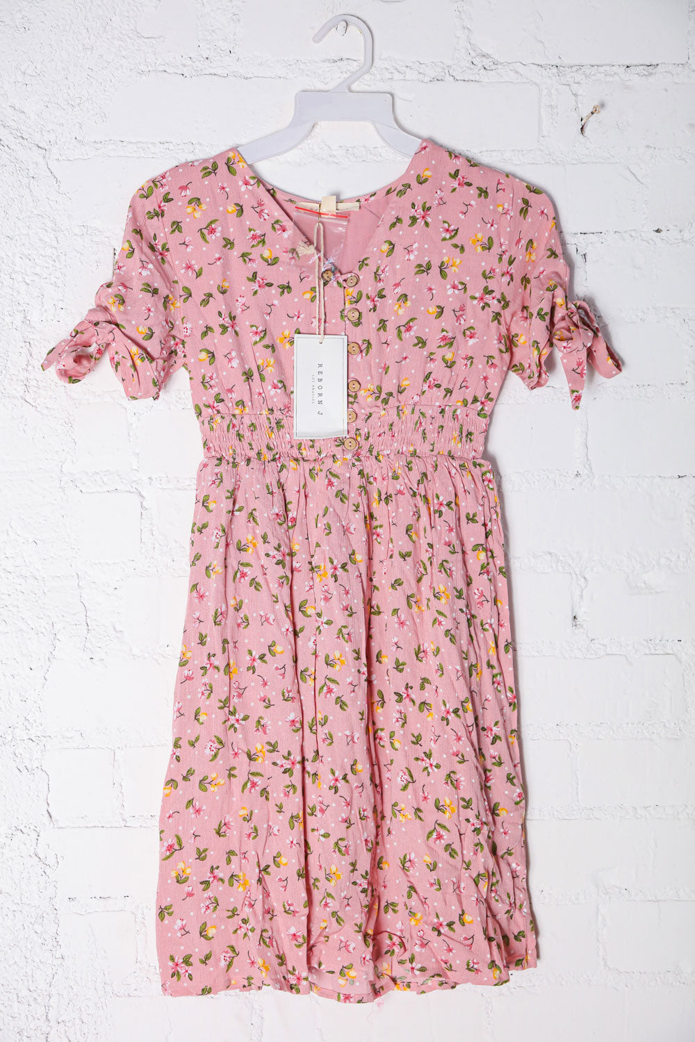 Kids Pink floral dress on a hanger against a white brick wall