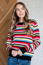 Woman wearing a colorful striped sweater against a white brick wall.