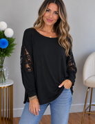 A black top with lace dolman sleeves, high V-neck, and a relaxed fit worn by a woman.