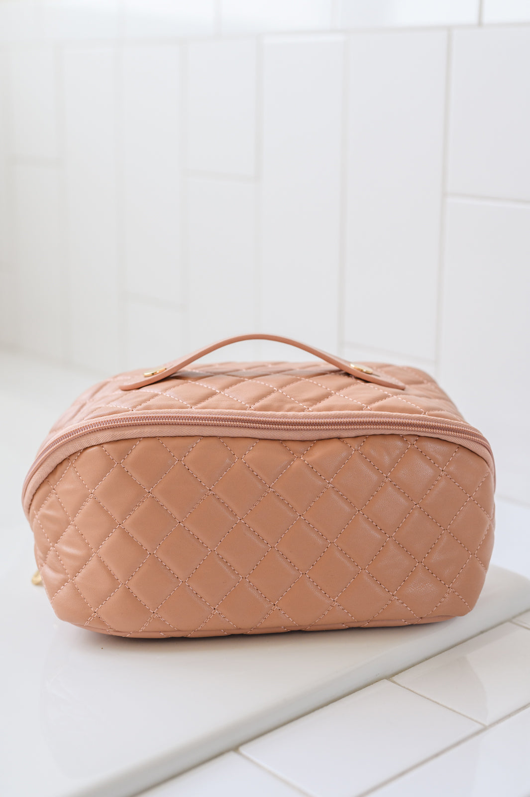 Pink quilted makeup bag with a side handle and gold accents on a white surface.